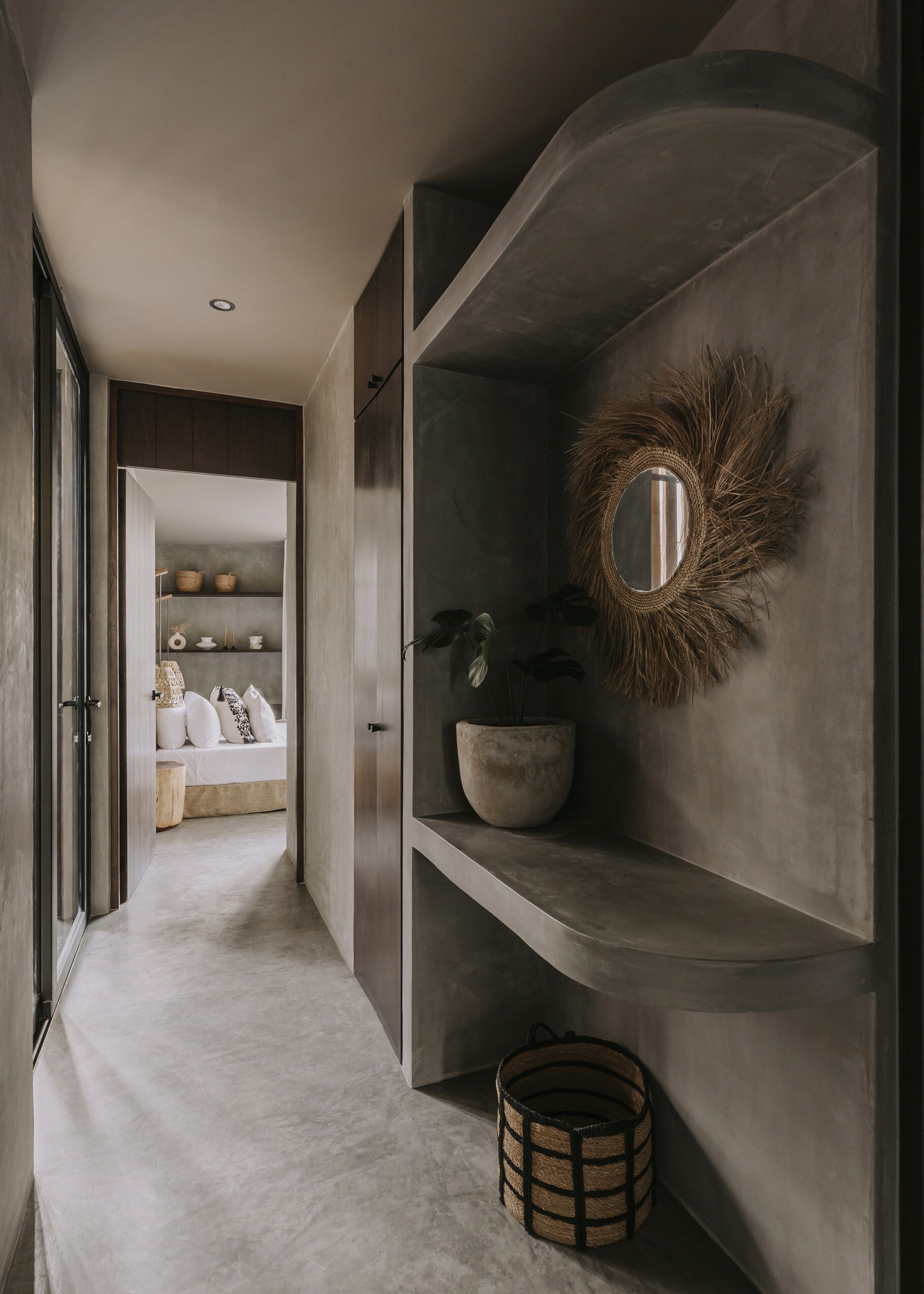A modern hallway with a minimalist design, featuring a curved mirror, a potted plant, and a woven basket on a shelf.