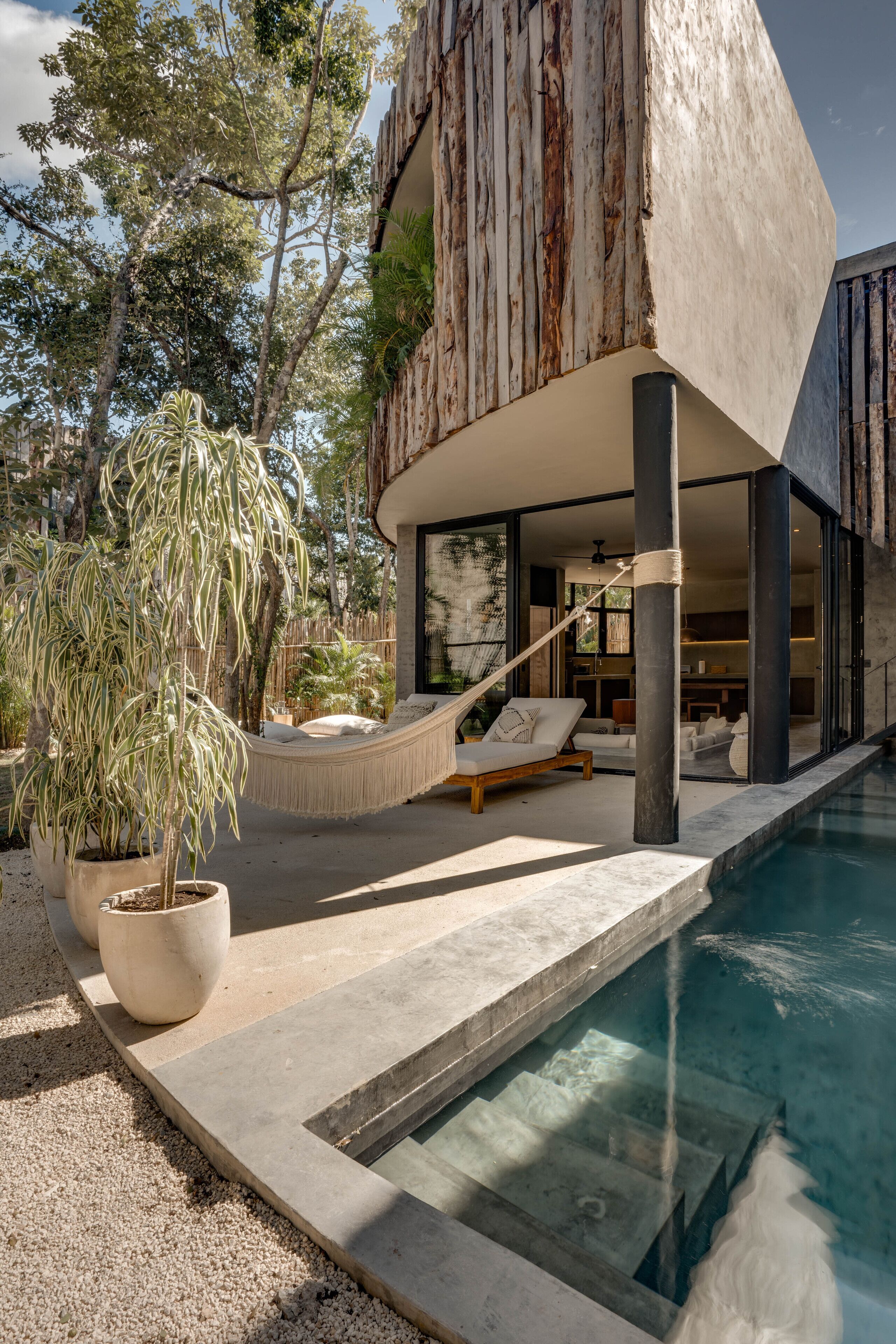 A modern outdoor pool area with a hammock, potted plants, and a view of the interior.