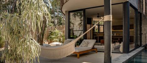 A modern outdoor pool area with a hammock, potted plants, and a view of the interior.