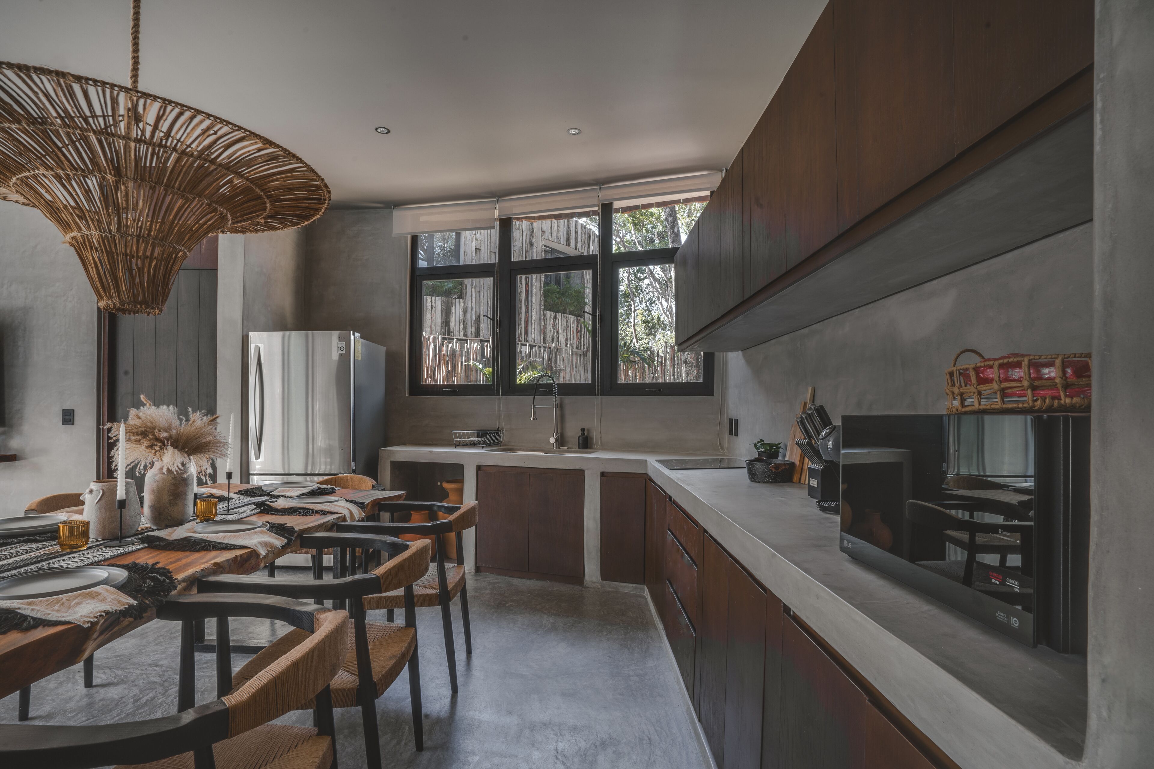 Une cuisine moderne dotée d’un grand îlot central, d’appareils électroménagers en acier inoxydable et d’un coin repas avec des chaises en bois et un chemin de table tissé.