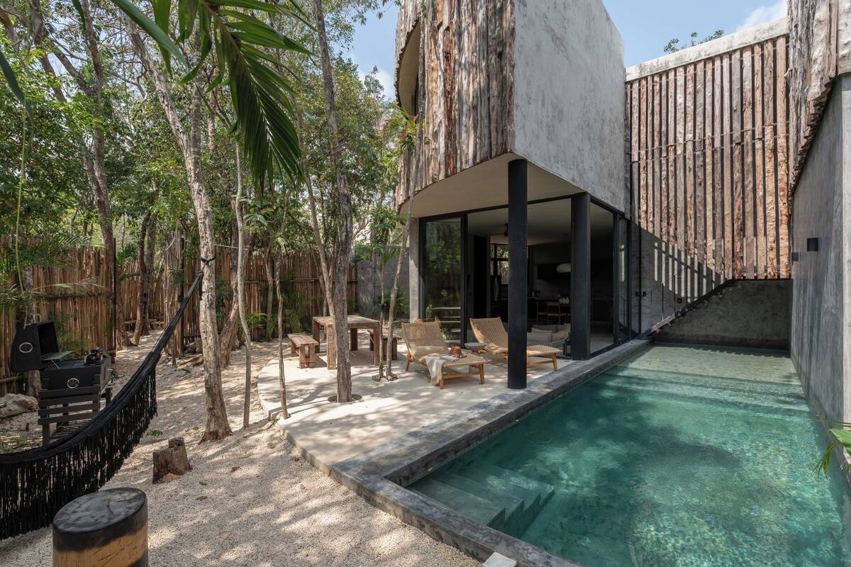 Uma área de piscina moderna ao ar livre, com piscina transparente, espreguiçadeiras de madeira e cercado de bambu.