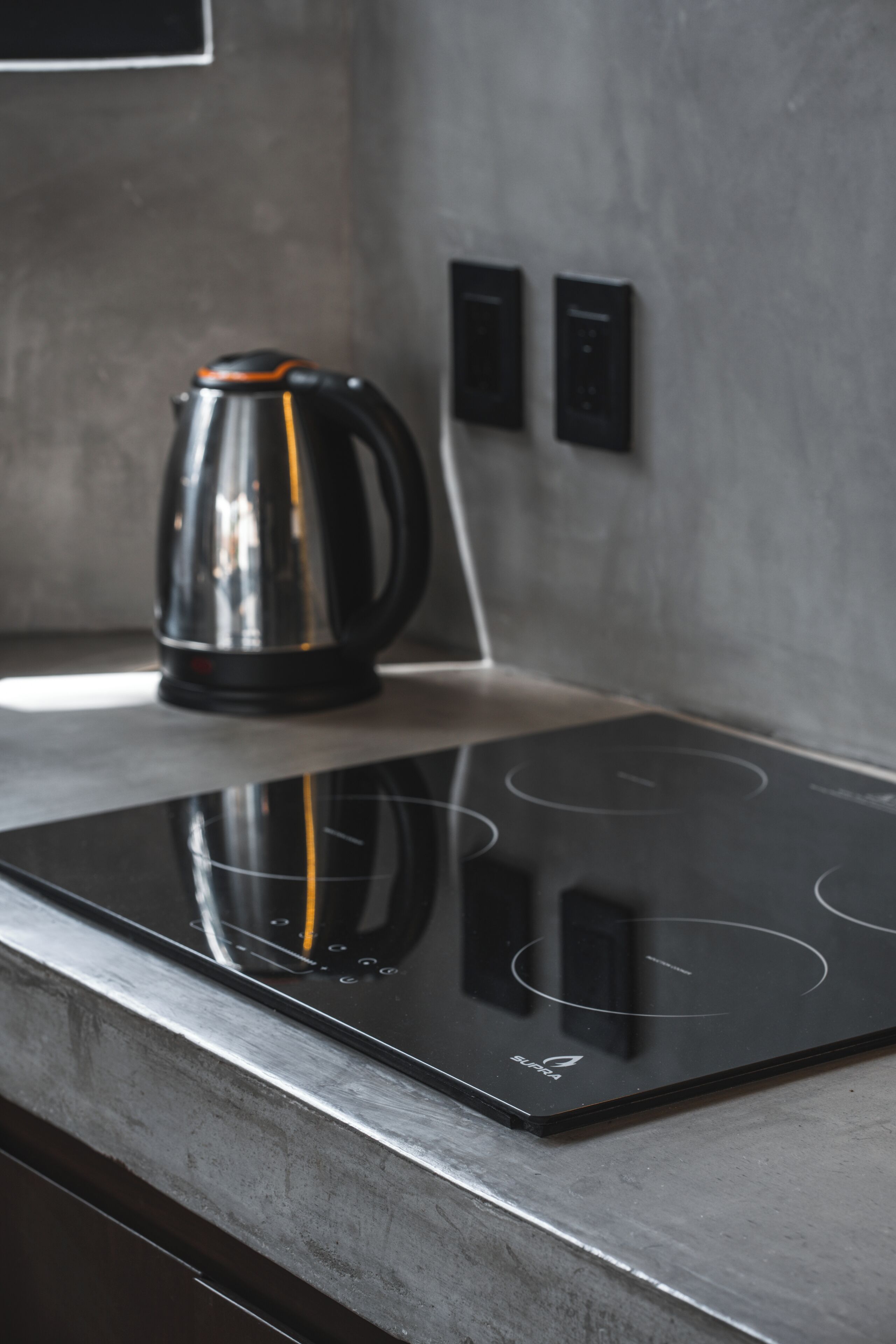 Une cuisine moderne dotée d’une plaque de cuisson à induction noire et d’une bouilloire en acier inoxydable.