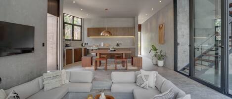Una sala de estar moderna con un sofá modular grande, una mesa de centro y una cocina al fondo.