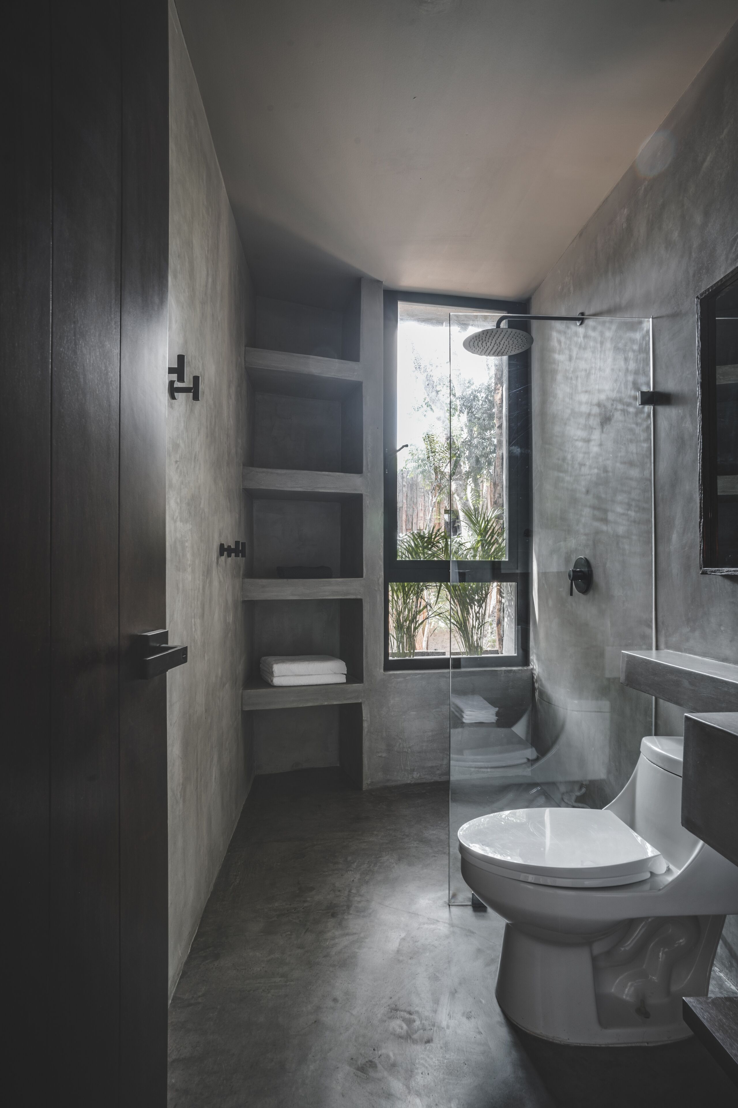 Ein modernes Badezimmer mit Toilette, Dusche und einem Fenster mit Blick auf Grünfläche.