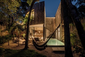 A modern outdoor pool area with a hammock, lounge chairs, and a dining area. - Esencia Villas (Tulum)