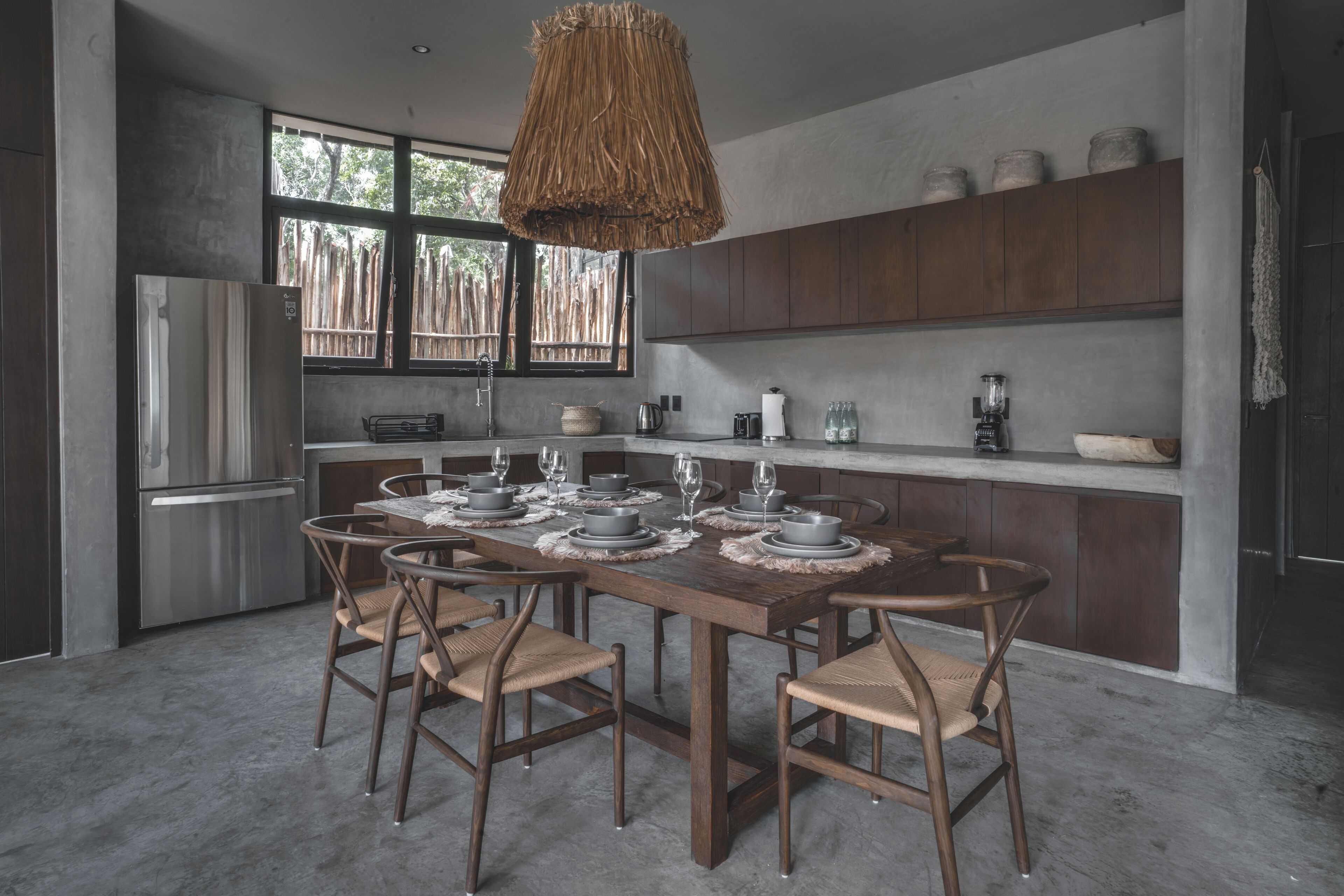 A modern kitchen with a wooden dining table set for six, equipped with a refrigerator, stove, and various kitchen appliances.