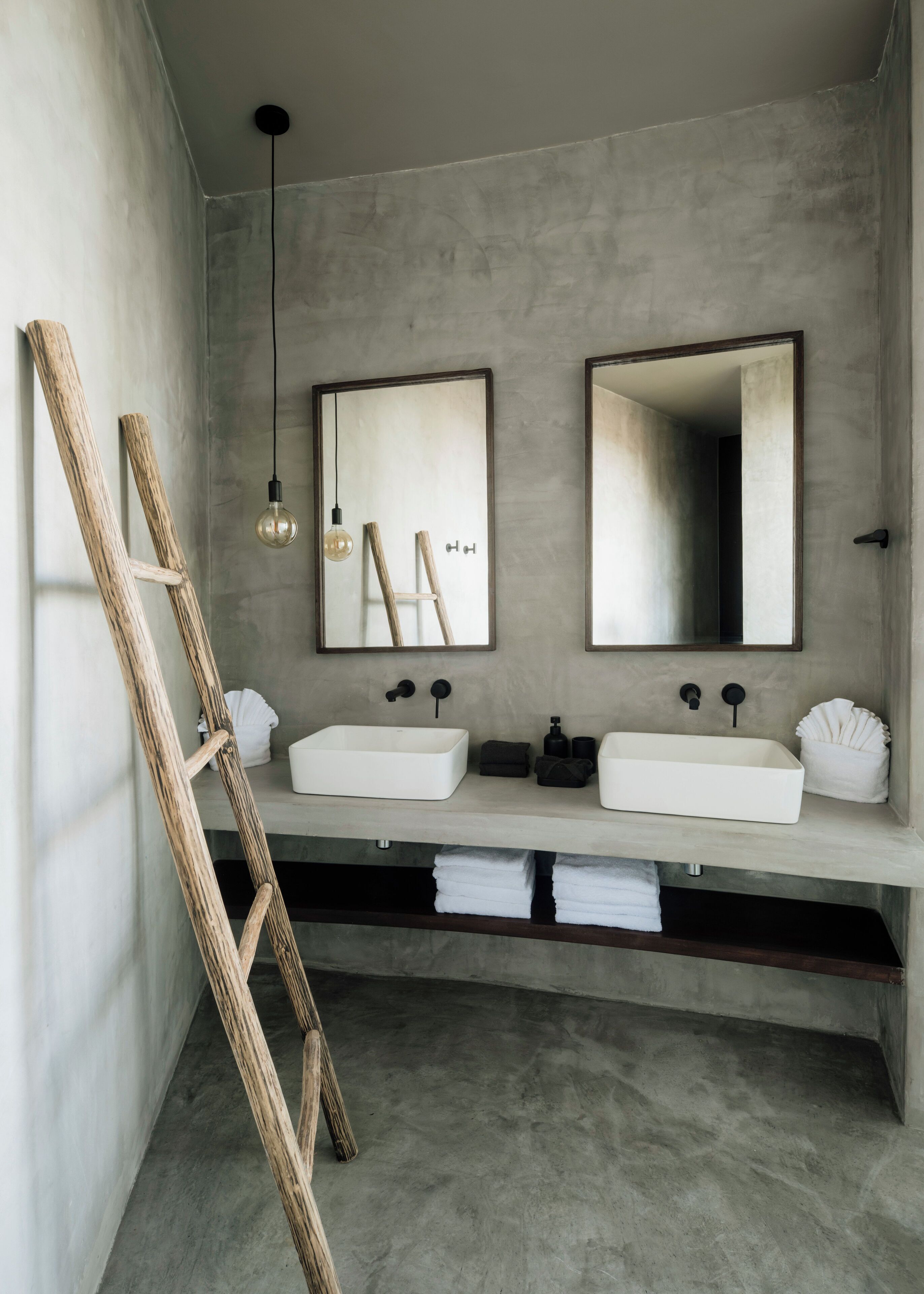 A modern bathroom with two white sinks, a wooden ladder, and a hanging light fixture.