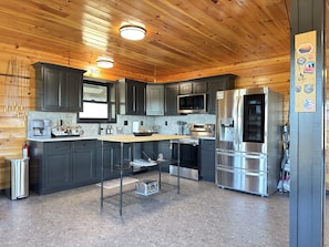A modern kitchen with dark cabinets, stainless steel appliances, and a wooden ceiling.
