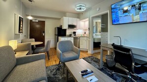 A compact living space with a kitchenette, a dining area, and a seating area with a TV. - The Gem Museum Suites (Evanston)