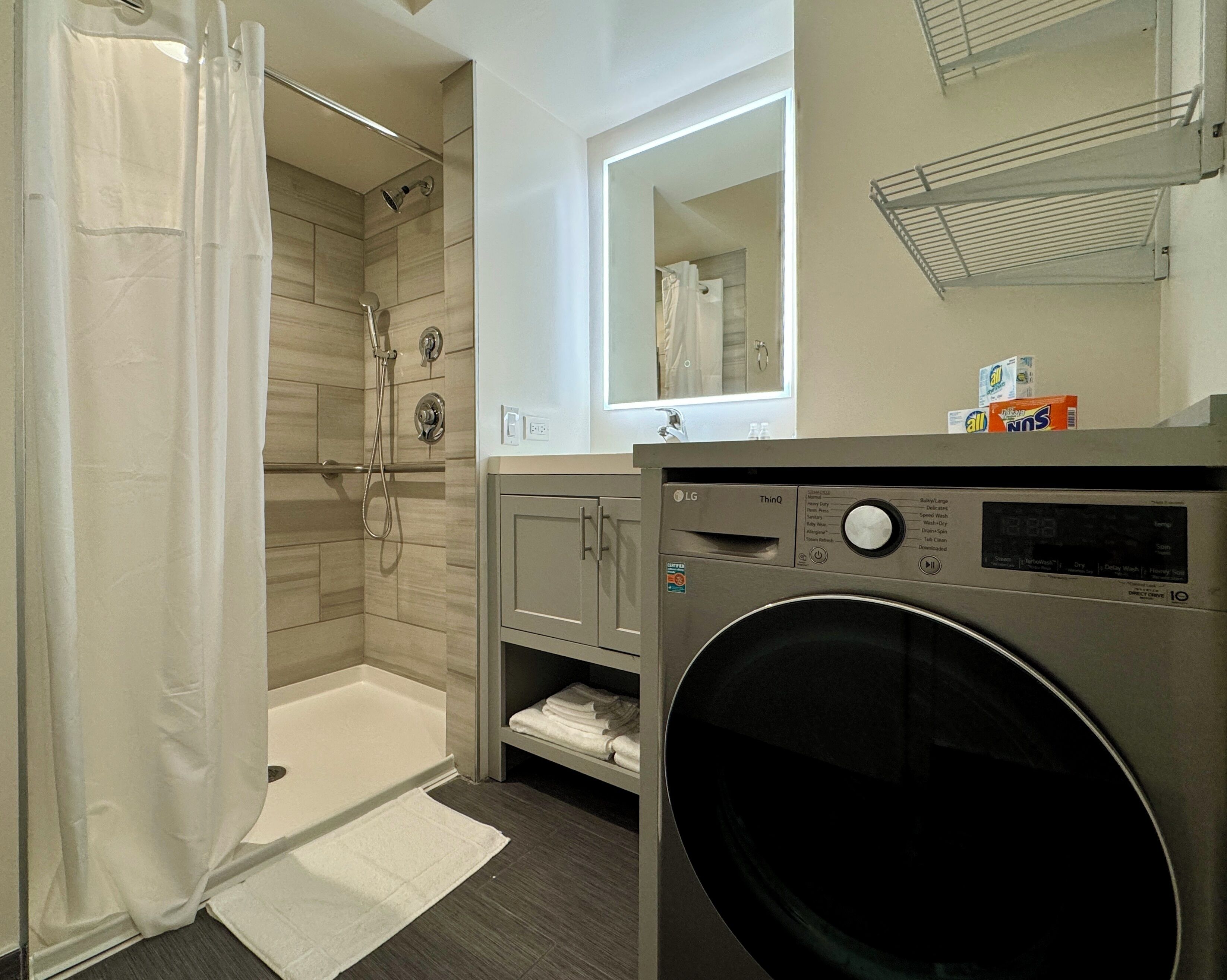 A modern bathroom with a walk-in shower, a built-in washing machine, and a mirror above the sink.