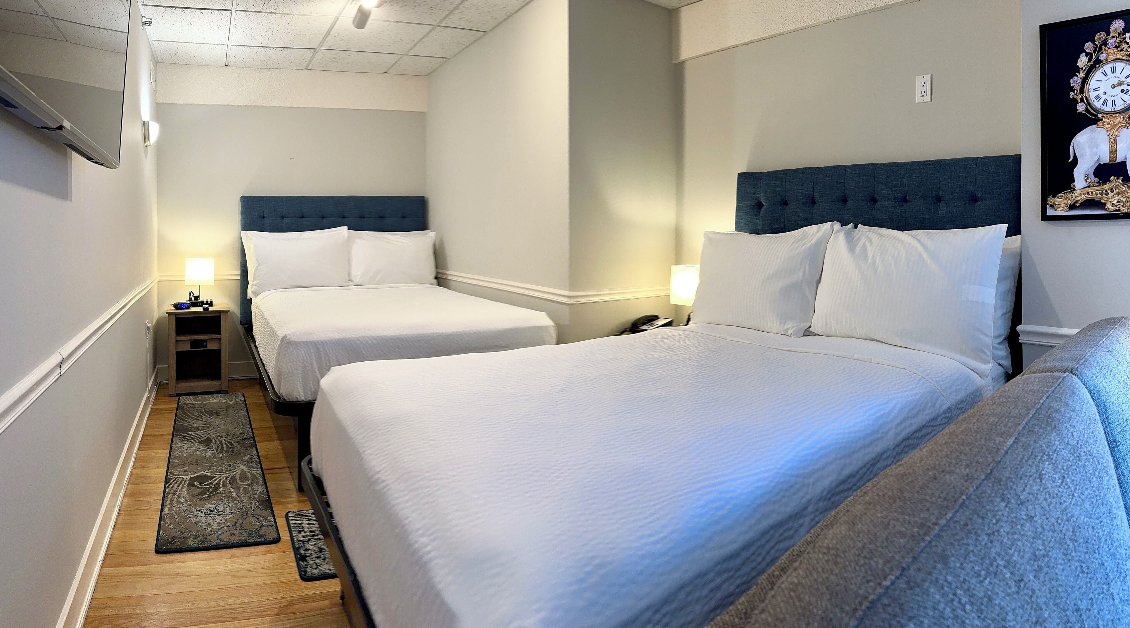 A hotel room with two beds, a nightstand, a lamp, and a framed picture on the wall.