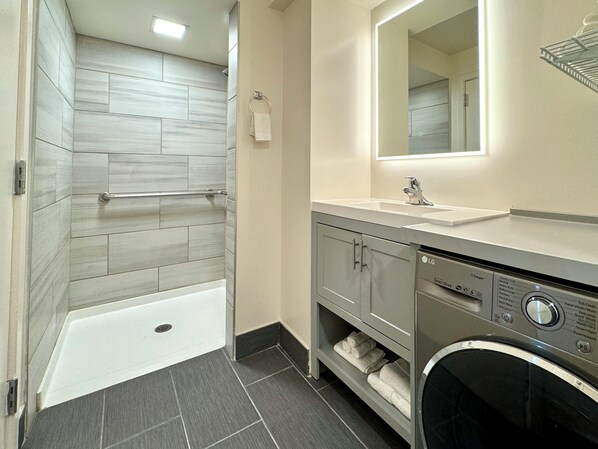 A modern bathroom with a walk-in shower, a built-in sink, and a washing machine.