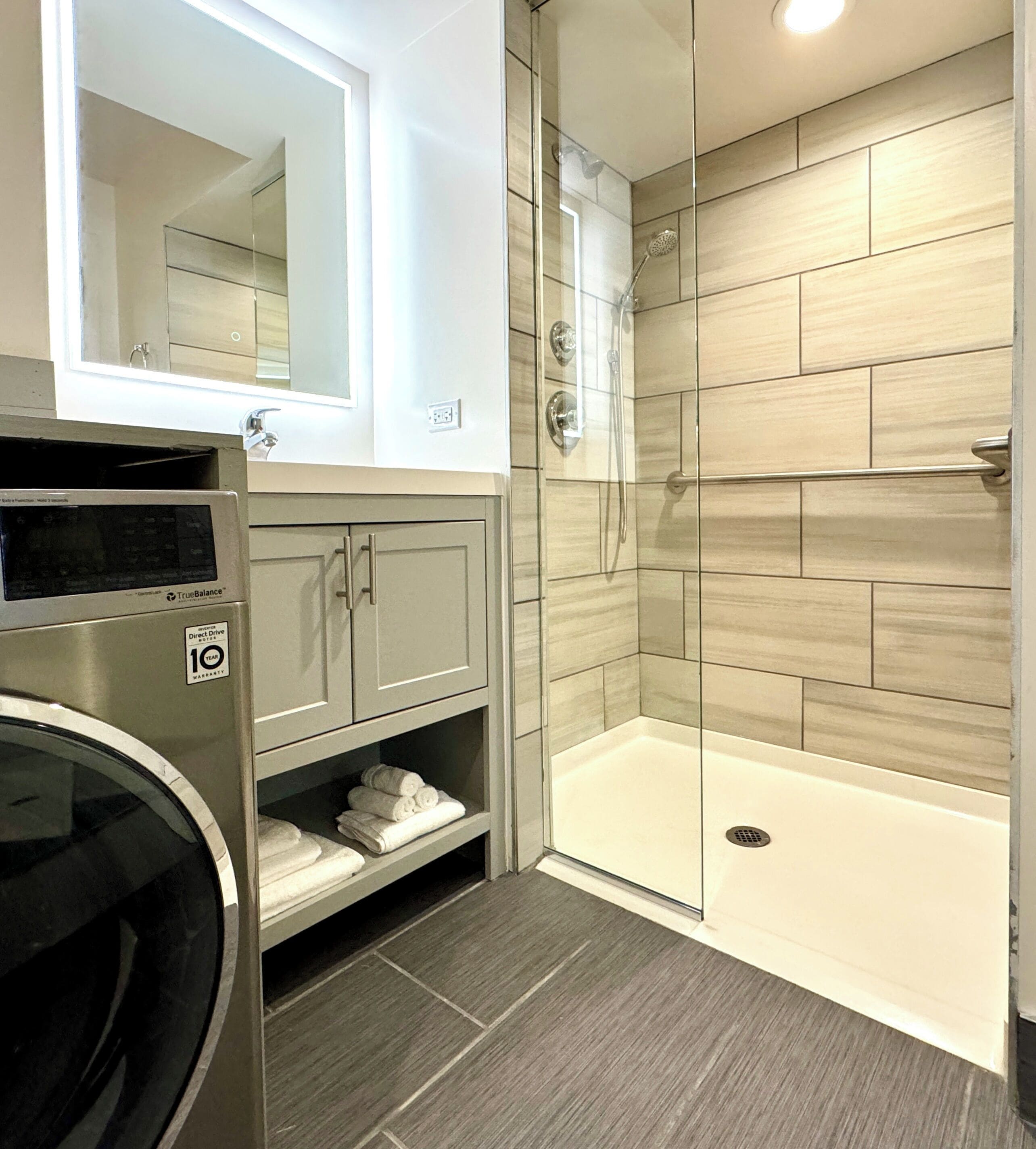 A modern bathroom with a built-in washer, a glass shower enclosure, and a bathtub.