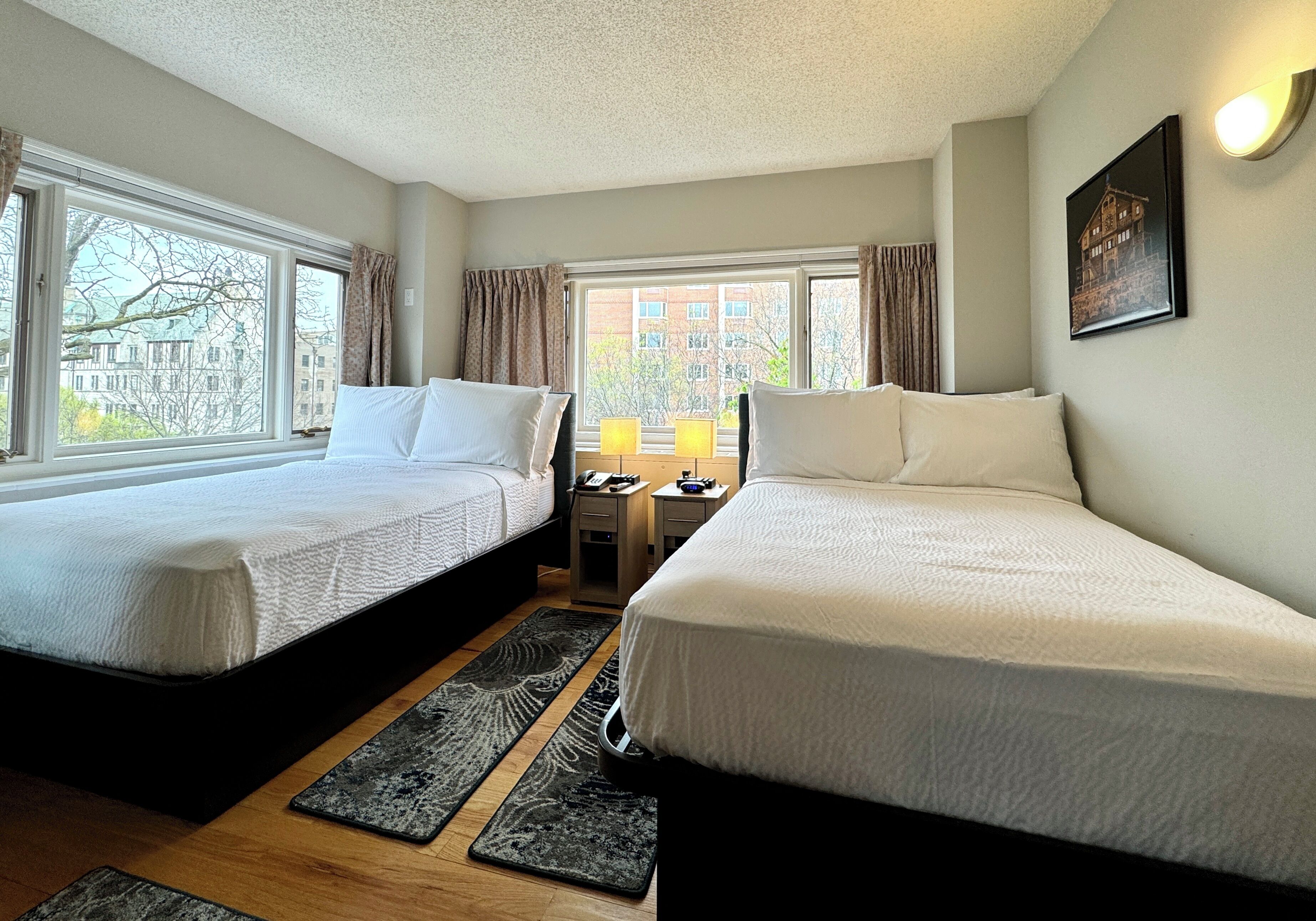 A hotel room with two beds, a desk with a lamp, and a window with curtains.