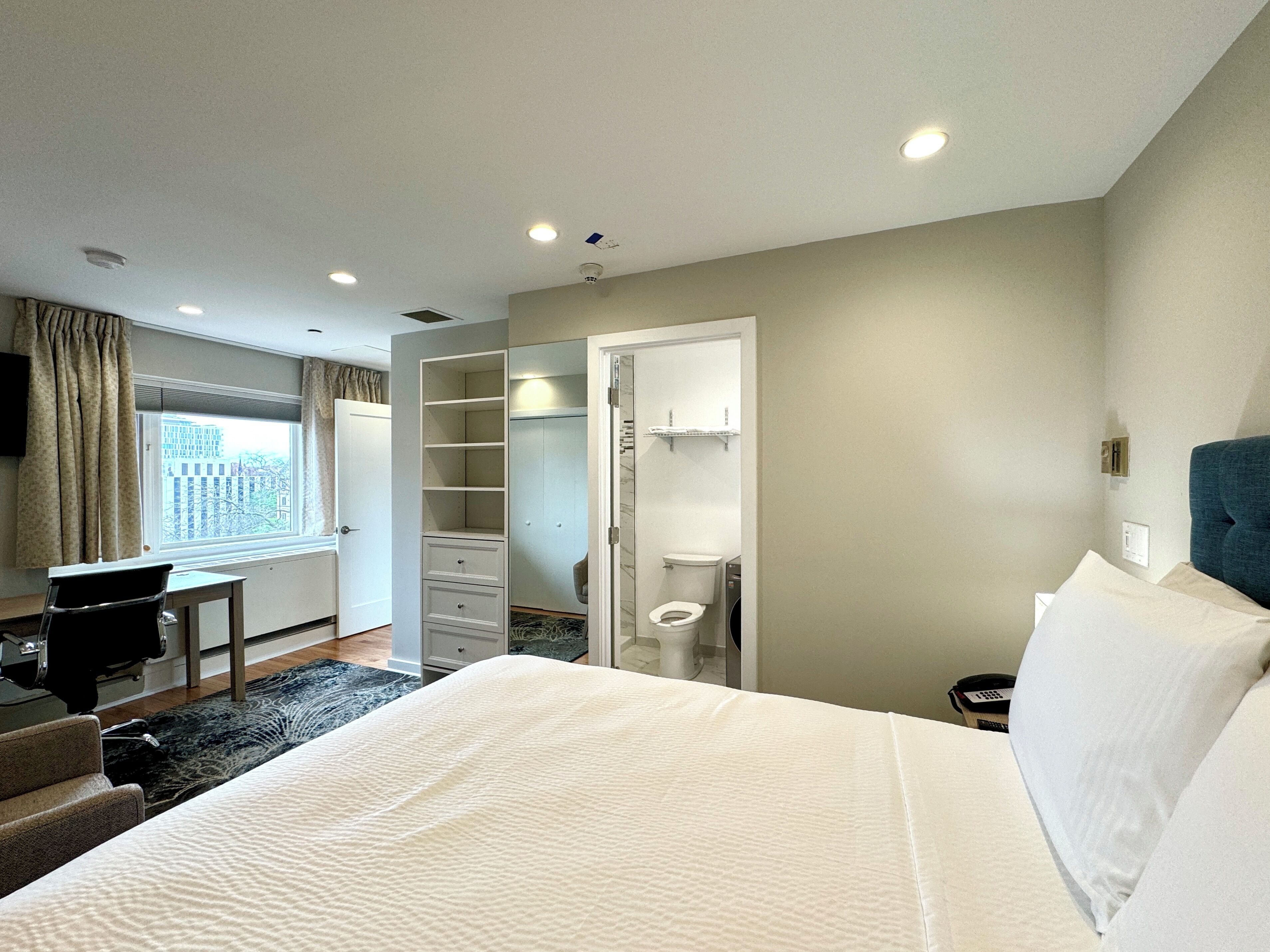 A hotel room with a bed, a desk, a chair, a closet, and a bathroom.