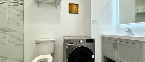 Une salle de bain moderne équipée de toilettes, d’un lave-linge et d’un meuble-lavabo avec un miroir.