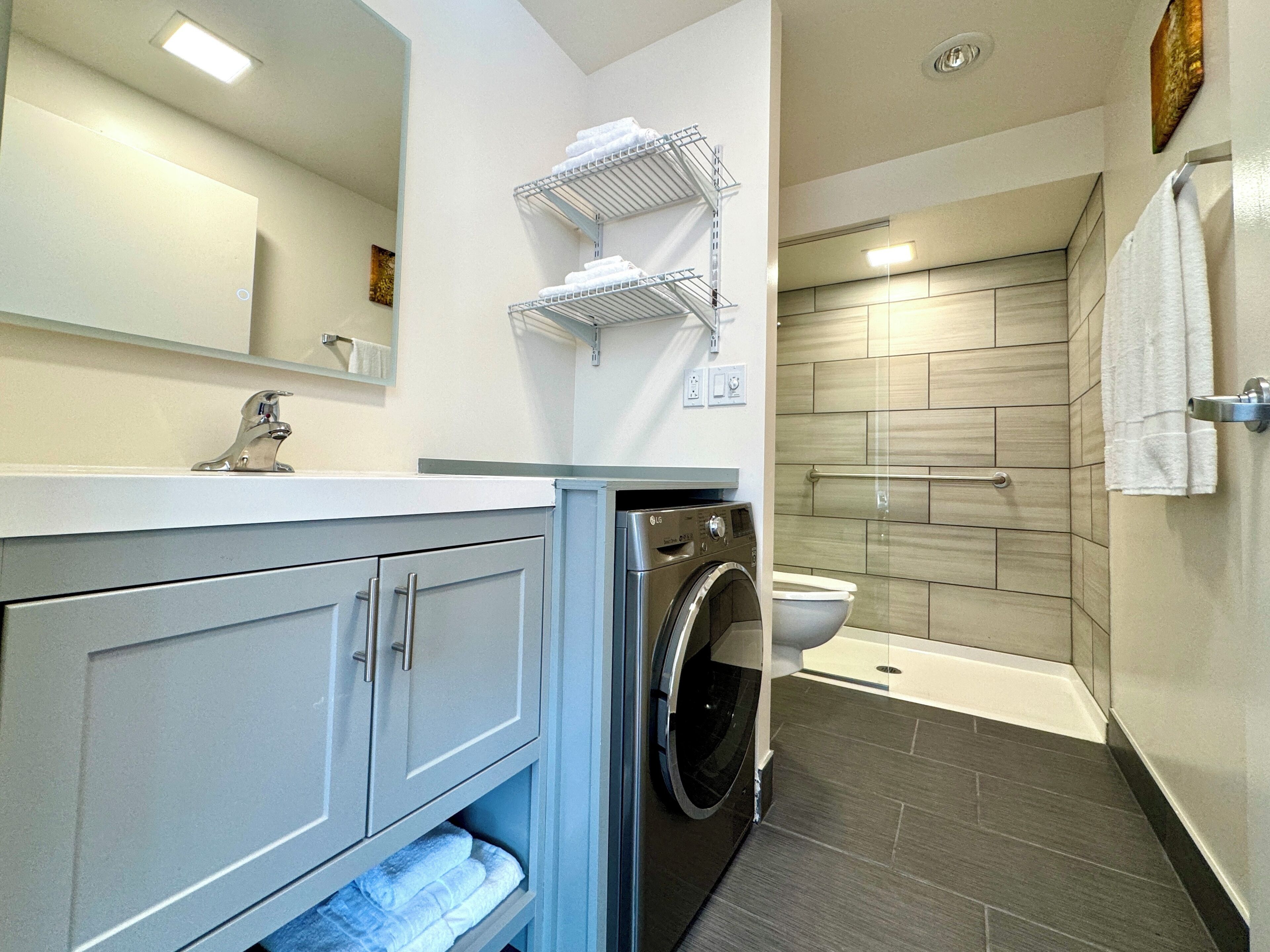 Une salle de bain moderne équipée d’un lave-linge et d’un sèche-linge intégrés, d’une douche avec une porte en verre et d’un porte-serviettes placé au-dessus du lavabo.