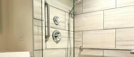 A modern bathroom with a glass shower enclosure, a bathtub, and a vanity with a towel rack.