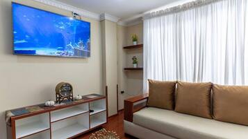 A living room with a flat-screen TV mounted on the wall, a sofa, a wooden console table, and a decorative plant.