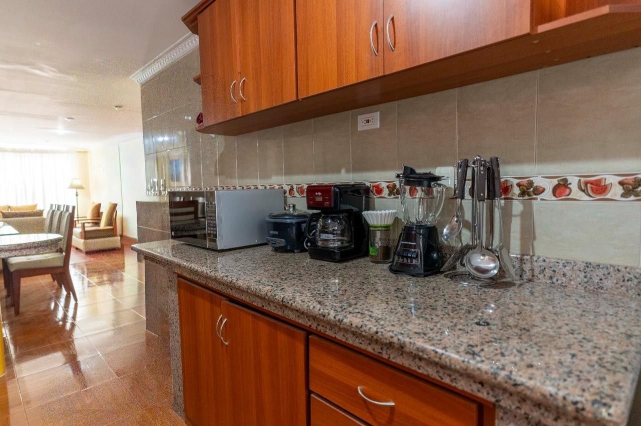 Una cocina con encimeras de granito, armarios de madera, cafetera, licuadora y tostadora.