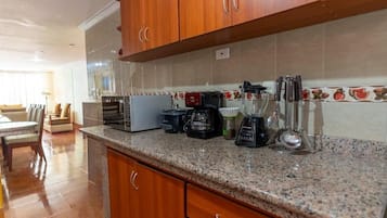 Una cocina con encimeras de granito, armarios de madera, cafetera, licuadora y tostadora.