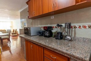 Une cuisine dotée de plans de travail en granit, d’armoires en bois, d’une machine à café, d’un mixeur et d’un grille-pain.