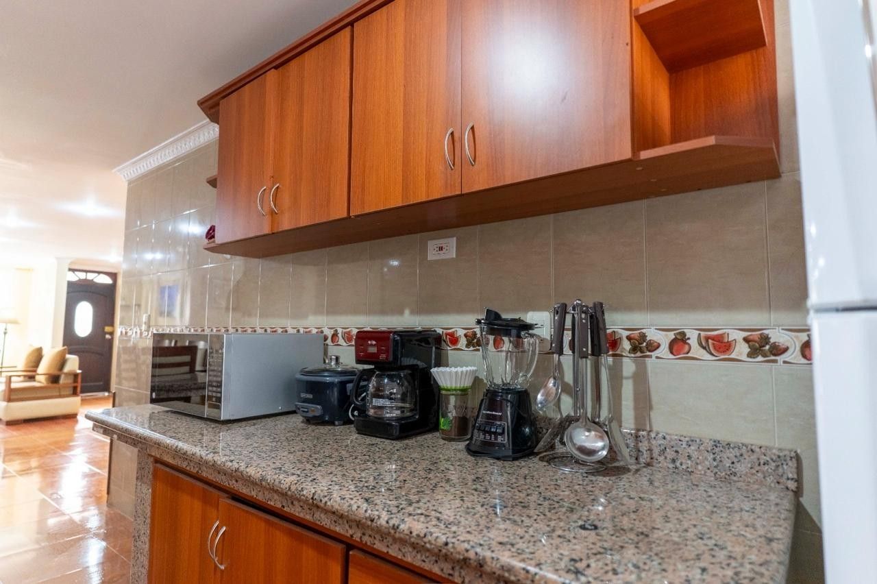 Una cocina con armarios de madera, encimera de granito y electrodomésticos varios, incluyendo cafetera y licuadora.