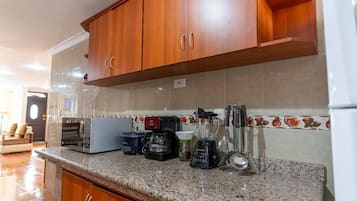 Una cocina con armarios de madera, encimera de granito y electrodomésticos varios, incluyendo cafetera y licuadora.