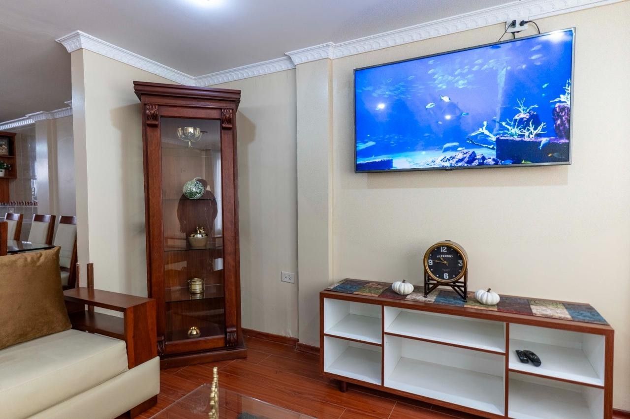 Ein Wohnzimmer mit einem Holzkabinett, einem an der Wand montierten Fernseher und einem Sofa.