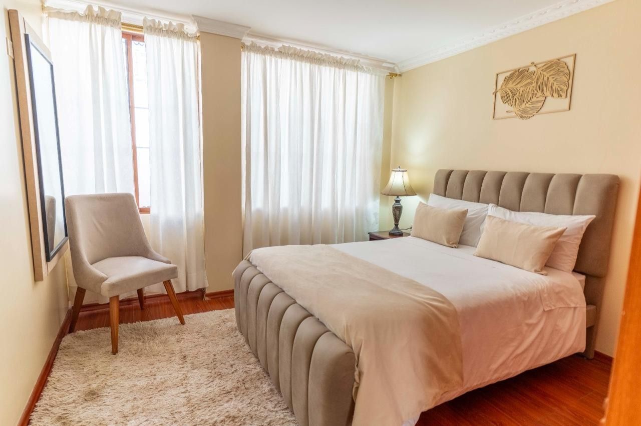 A bedroom with a bed, a chair, a lamp, and a framed picture on the wall.