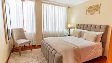 A bedroom with a bed, a chair, a lamp, and a framed picture on the wall.