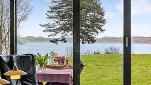 A dining area with a table set for two, overlooking a lake with a large tree in the background. - Awesome home in Roslev with kitchen (Roslev)