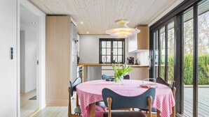 A dining area with a table set for two, a wooden ceiling, and a view of the outdoors through large windows. - Awesome home in Roslev with kitchen (Roslev)