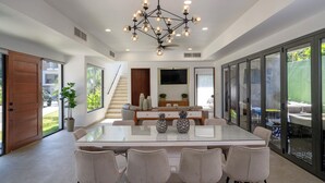 A modern dining area with a glass table and chairs, a chandelier, and a view of the outdoors. - Brand New Luxury Villa on the South End of Jaco Beach, Steps from the Beach! (Jaco)