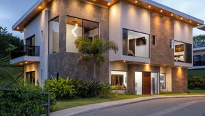Une maison moderne à deux étages, dotée d’un toit plat, de grandes fenêtres et d’un jardin bien entretenu.