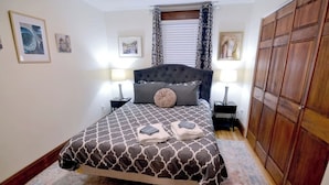 A neatly arranged bedroom with a large bed, two bedside tables, a wardrobe, and framed artwork on the walls. - Bedford Bungalow (Bedford)