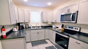 A modern kitchen with white cabinets, a stainless steel microwave, a stove, and a sink. - Bedford Bungalow (Bedford)
