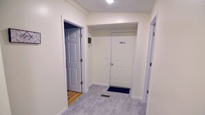 A hallway with a wooden floor, white walls, and a door with a 'No Parking' sign. - Bedford Bungalow (Bedford)