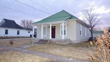 A single-story house with a green roof, a front porch, and a mailbox.