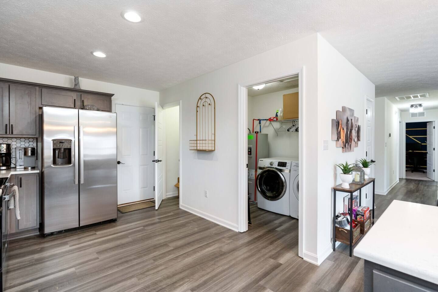 A modern kitchen with stainless steel appliances, a laundry area with a washing machine, and a hallway leading to a living space.