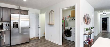 A modern kitchen with stainless steel appliances, a laundry area with a washing machine, and a hallway leading to a living space.