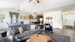 Ein modernes Wohnzimmer mit grauem Sofa, blauen Sessel und einem Couchtisch aus Holz, sowie einem Deckenventilator.
