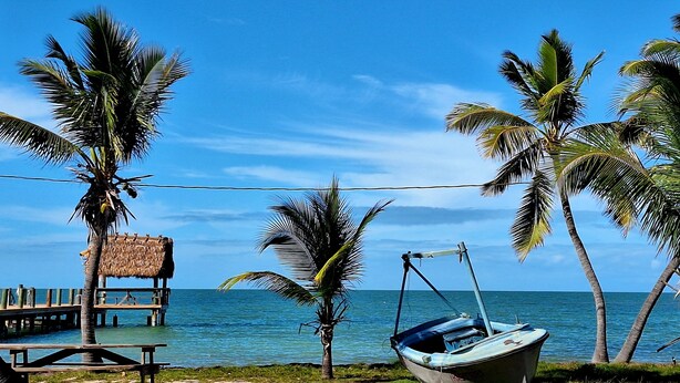 A beach with a thatched-roof hut, a wooden bench, and a boat. - Luxury Pull Thru Rv lot with access to all the Resorts amenities!  (Cudjoe Key)