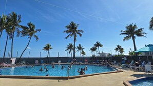 A swimming pool with people swimming and sunbathing, surrounded by palm trees and lounge chairs. - Luxury Pull Thru Rv lot with access to all the Resorts amenities!  (Cudjoe Key)