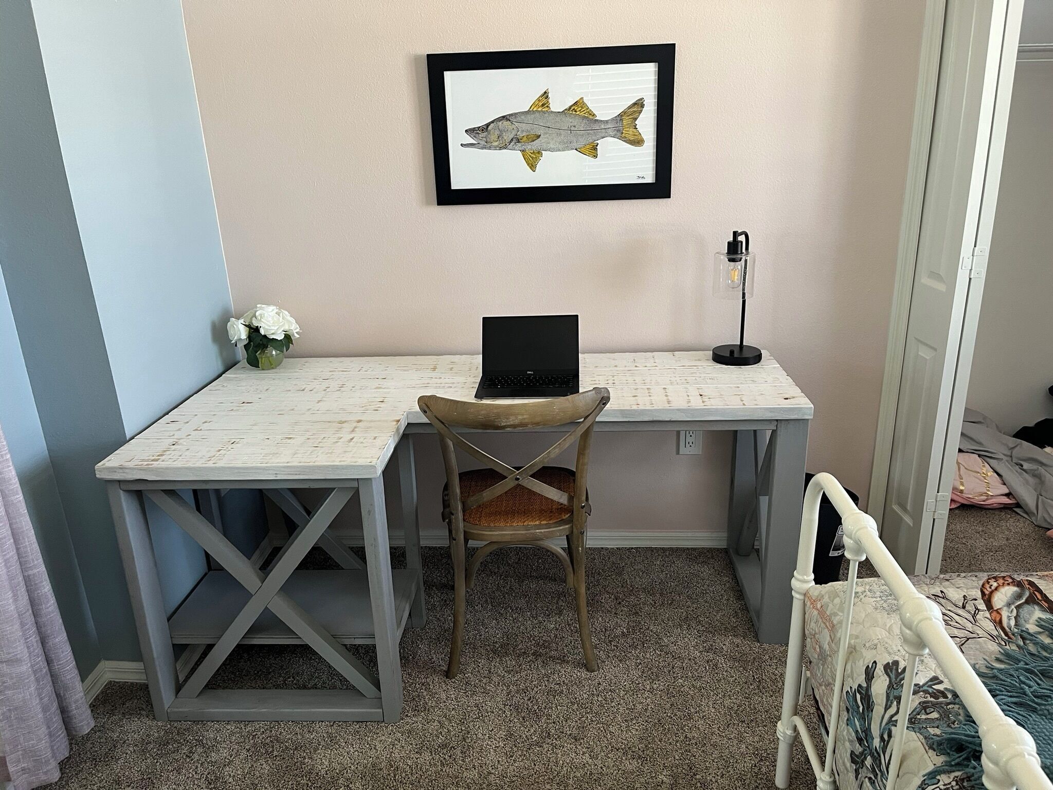 A room with a desk, a laptop, a framed fish picture, a small plant, and a bed with a blanket.
