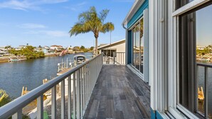 Un balcon avec vue sur une rivière, un palmier et un quai.