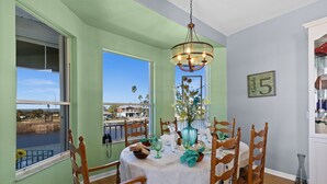 Un coin repas avec une table dressée pour quatre personnes, entouré de chaises en bois, d’un lustre et offrant une vue sur une étendue d’eau grâce à de grandes fenêtres.