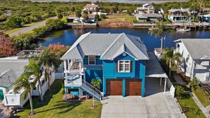 Une maison située sur la côte, avec une façade bleue, un garage et une jetée qui s’avance dans une baie tranquille.