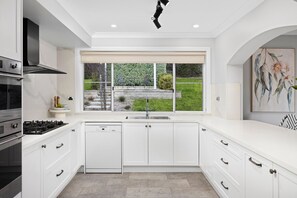 A modern kitchen with white cabinetry, a built-in dishwasher, a gas stove, and a window with a view of a garden.