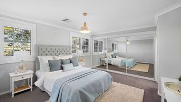 A bedroom with a large bed, bedside tables, a mirror, and a window with blinds.